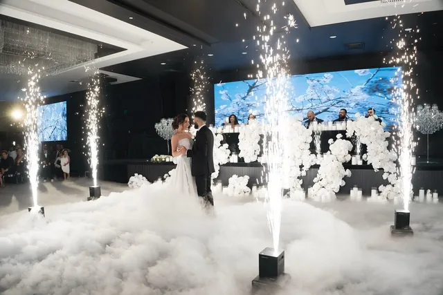 Bride and groom sharing a first dance on low lying clouds with sparkler fountains and an LED wall