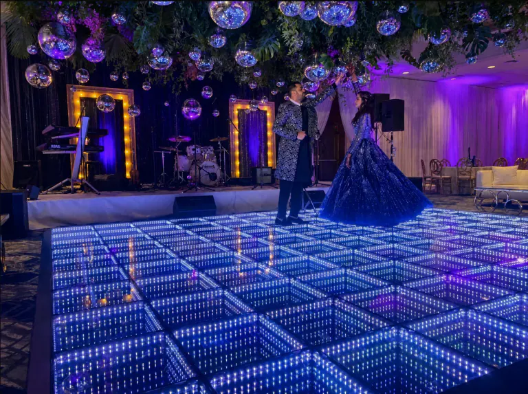 Couple standing together on an infinity LED dance floor beneath hanging mirror balls