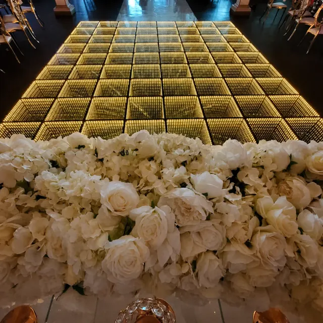 Golden infinity LED dance floor framed by white florals