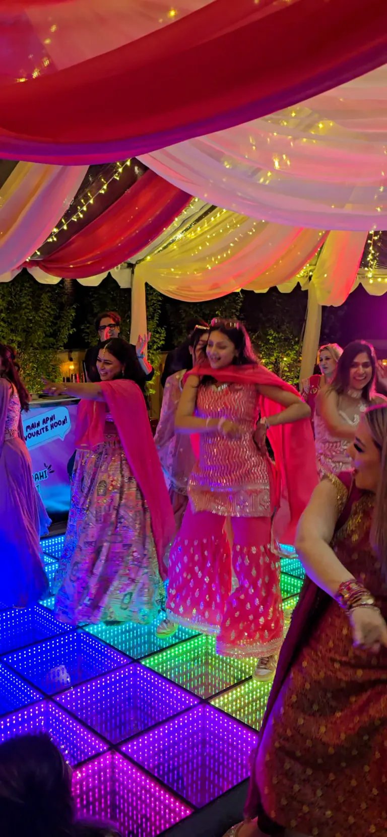 Wedding guests dancing on a colorful infinity LED floor under a draped tent
