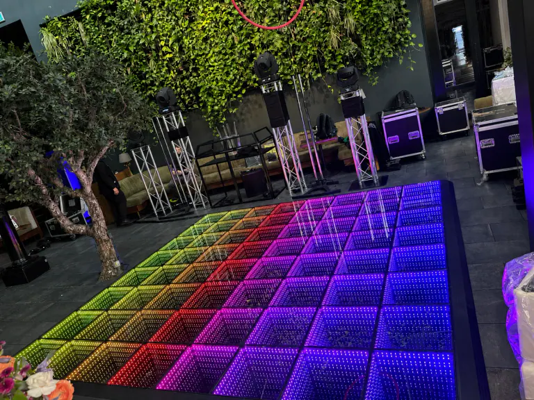 Rainbow infinity LED dance floor in front of a green foliage wall